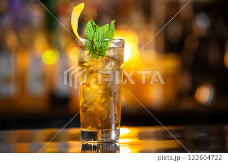 Closeup glass of cuba libre cocktail decorated with mint at orange lighted bar counter background. Closeup glass of cuba libre cocktail decorated with mint at orange lighted bar counter background. 122604722