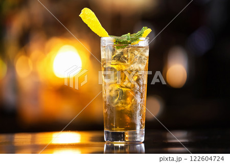 Closeup glass of long island ice tea cocktail decorated with mint at orange lighted bar counter background. Closeup glass of long island ice tea cocktail decorated with mint at orange lighted bar counter background. 122604724