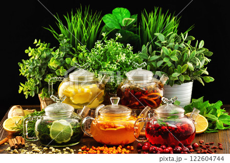 Set of colorful glass tea pots decorated with green plants and berries on a wooden table board at dark background. 122604744