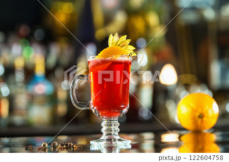Closeup glass of red cocktail decorated with orange and apple slices at bright bar counter background. Closeup glass of red cocktail decorated with orange and apple slices at bright bar counter background. 122604758
