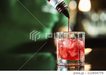 Closeup image of pouring syrup from buttle to cocktail glass at bar background. 122604779