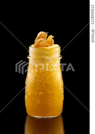 Glass jar of fresh yellow mango and orange smoothie decorated with winter cherry isolated at black background. Glass jar of fresh yellow mango and orange smoothie decorated with winter cherry isolated at black background. 122604812