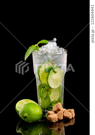 Closeup vertical glass of mojito cocktail decorated with lime, cane sugar and mint isolated at black background. 122604941