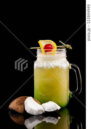 Jar with homemade lemonade with pineapple, coconut and lemon decorated with cherry isolated at black background. Jar with homemade lemonade with pineapple, coconut and lemon decorated with cherry isolated at black background. 122604949