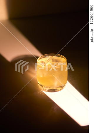Closeup shining glass of cocktail at minimal dark background with light stripes and golden reflections. 122604960
