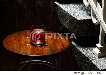 Closeup glass of negroni cocktail with ice at bar table at porch stairs background. Closeup glass of negroni cocktail with ice at bar table at porch stairs background. 122604972