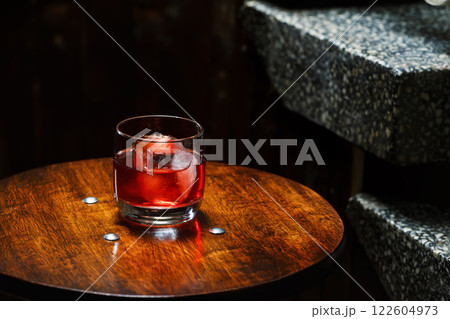 Closeup glass of negroni cocktail with ice at bar table at porch stairs background. Closeup glass of negroni cocktail with ice at bar table at porch stairs background. 122604973