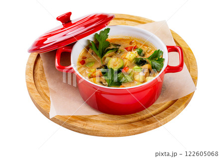 Red pot of healthy vegetarian soup with potatoes, squash, carrot and romatoes served at a wooden board isolated at white background. Red pot of healthy vegetarian soup with potatoes, squash, carrot and romatoes served at a wooden board isolated at white background. 122605068