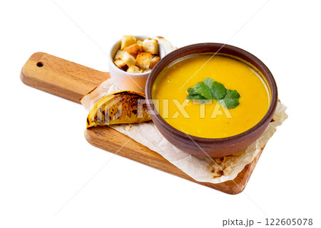 Clay bowl of pumpkin creme soup served with orange slice at wooden tray isolated at white background. 122605078