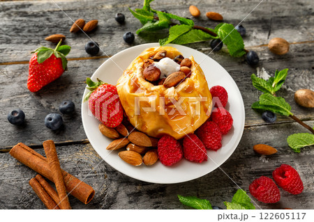 Closeup plate of stuffed baked apple dessert served with strawberries, raspberries, blueberries, mint and cinnamon at wooden table background. Closeup plate of stuffed baked apple dessert served with strawberries, raspberries, blueberries, mint and cinnamon at wooden table background. 122605117