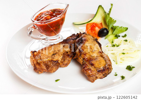 Grilled pork shashlik with red spicy sauce and vegetables on plate isolated at white background. Grilled pork shashlik with red spicy sauce and vegetables on plate isolated at white background. 122605142