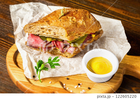 Closeup image of sandwich with meat and cucumbers at wooden board background. Closeup image of sandwich with meat and cucumbers at wooden board background. 122605220