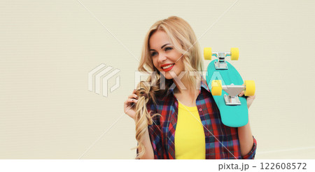 Stylish young blonde woman posing with skateboard on city street 122608572
