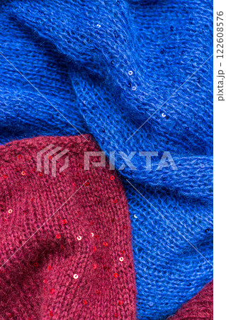 Red and blue knitted sweater with sequins. Sequinned knitwear. Sequin pattern in needlework. Knitting hobby. Knitter work. Sequins texture in knitwear. Bright knitted fashion for holidays. 122608576
