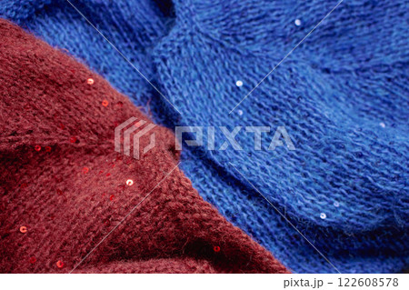 Red and blue knitted sweater with sequins. Sequinned knitwear. Sequin pattern in needlework. Knitting hobby. Knitter work. Sequins texture in knitwear. Bright knitted fashion for holidays. 122608578
