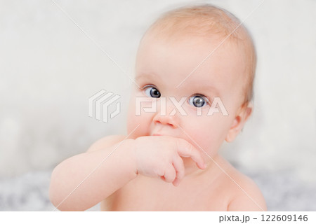 Close-up of baby with blue eyes and fair skin sucking their thumb and making playful scrunched-up facial expression. concepts related to childhood, emotions, teething, curiosity and early development. Close-up of baby with blue eyes and fair skin sucking their thumb and making playful scrunched-up facial expression. concepts related to childhood, emotions, teething, curiosity and early development. 122609146