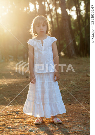 Portrait of  brunette child girl in white clothes standing on the background of the sunny park 122609147