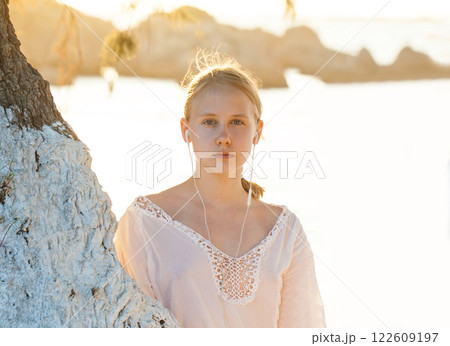 Blonde beautiful teenage girl stand near tree and listen to music in headphones  122609197