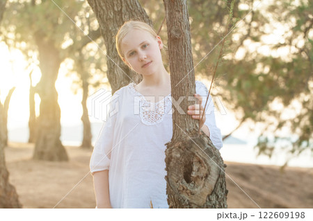 Beautiful teenage girl in white shirt and skirt on the background of forest and sunlight Beautiful teenage girl in white shirt and skirt on the background of forest and sunlight 122609198
