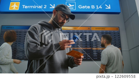 Airport Terminal: Man with Backpack Checks Flight Information Scanning Ticket Using Phone Airport Terminal: Man with Backpack Checks Flight Information Scanning Ticket Using Phone 122609558