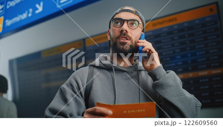 Airport Terminal: Male Passenger Holding Plane Ticket, Talking by Phone Airport Terminal: Male Passenger Holding Plane Ticket, Talking by Phone 122609560