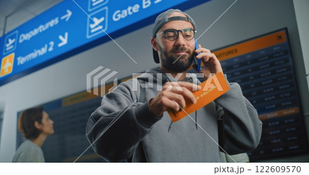 Airport Terminal: Man Holding Plane Ticket, Talking by Phone to Check Information 122609570