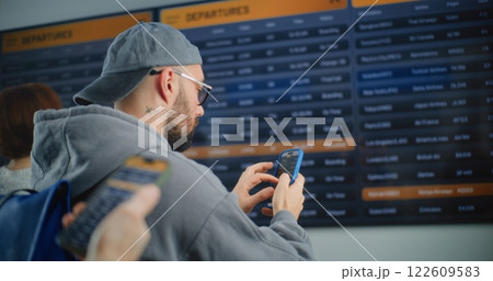 Male Passenger Looking for Flight on Digital Arrival and Departure Information Board, Using Phone Male Passenger Looking for Flight on Digital Arrival and Departure Information Board, Using Phone 122609583
