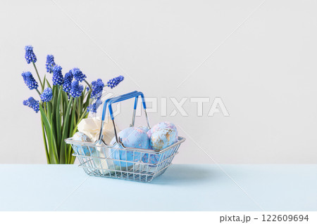 Painted blue Easter eggs and a small gift box in a metal basket on a blue table and a bouquet of spring blue muscari flowers. Easter concept Painted blue Easter eggs and a small gift box in a metal basket on a blue table and a bouquet of spring blue muscari flowers. Easter concept 122609694