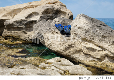 Snorkeling gear resting on rocky shore near clear turquoise waters on a sunny day Snorkeling gear resting on rocky shore near clear turquoise waters on a sunny day 122610133