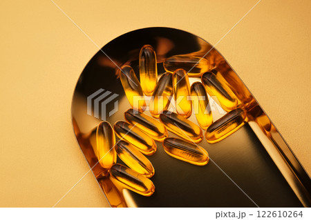 Yellow capsules with Omega-3 fish oil on a golden tray. 122610264