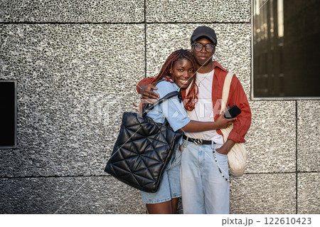 Happy African American siblings cuddlling, look at camera with smiles near wall. Weekend stroll 122610423