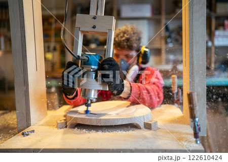 Joiner shaping stool base on drilling cnc machine in workshop. Furniture smoothing, production 122610424