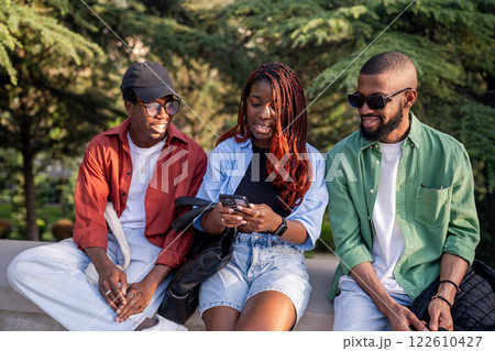 Lively African American friend sit in park, phone in hand. Woman shares trending social media post 122610427