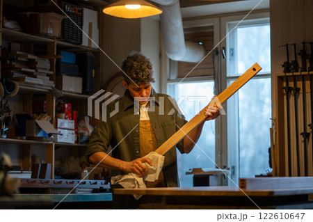 Serious focused male carpenter working preparing wooden block polishes removes dust with towel. Serious focused male carpenter working preparing wooden block polishes removes dust with towel. 122610647