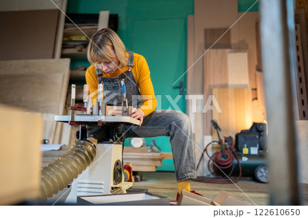 Female carpenter turn wood on lathe, shape custom pieces in workshop. Skilled labor, custom orders 122610650