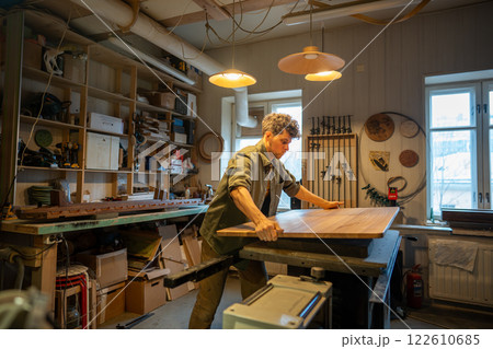 Skilled joiner crafts custom wooden table from solid wood in shop workshop. Handcrafted quality 122610685