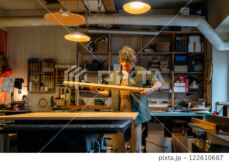 Focused woodworker examines table components before finishing assembly in carpentry workshop Focused woodworker examines table components before finishing assembly in carpentry workshop 122610687