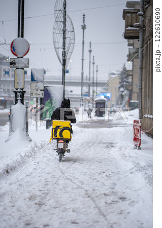 Winter food deliver service. Rear view of person deliver on electric scooter in snowfall Winter food deliver service. Rear view of person deliver on electric scooter in snowfall 122610690