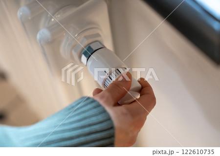 Hand turning radiator valve reducing temperature in flat, private house to save, economize energy 122610735