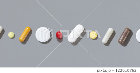 Mix of medical capsules and pills in a line on grey top view, hard shadow. Pharmaceutical products Mix of medical capsules and pills in a line on grey top view, hard shadow. Pharmaceutical products 122610762