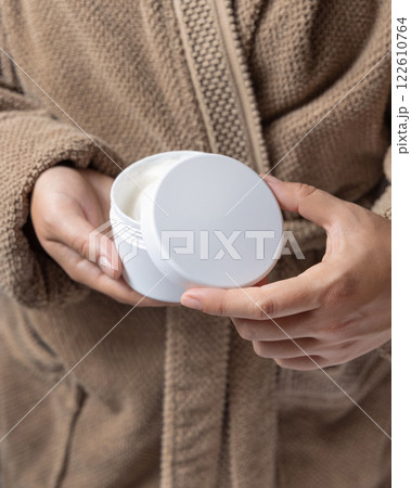 Closeup of woman in brown bathrobe opening white cream jar with hands, cosmetic mockup Closeup of woman in brown bathrobe opening white cream jar with hands, cosmetic mockup 122610764