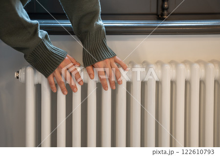 Woman warming hands near radiator at home after walking in cold winter weather, closeup Woman warming hands near radiator at home after walking in cold winter weather, closeup 122610793