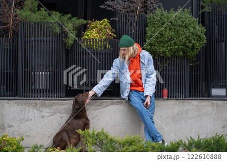 Kind stylish hipster guy in trendy outfit caressing street dog, playing, amusing homeless pet 122610888