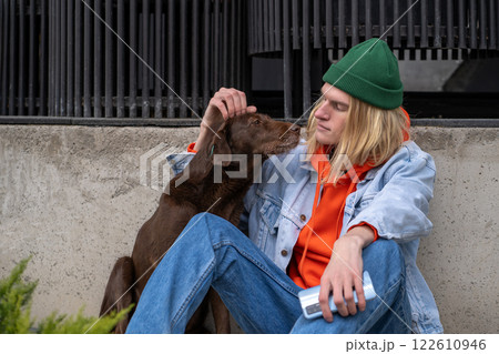 Kind young man hipster stroking stray street dog sitting outside. Compassion to homeless animals. 122610946