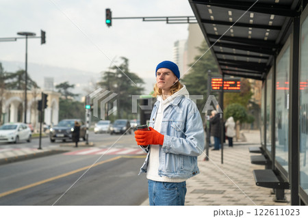 Pensive stylish trendy hipster guy with coffee look into distance, waiting for taxi, bus at bus stop Pensive stylish trendy hipster guy with coffee look into distance, waiting for taxi, bus at bus stop 122611023