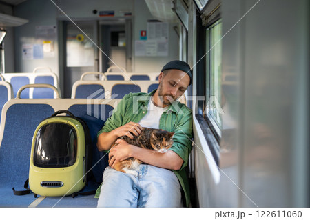 Public electric train ride of thoughtful man hugging calm peaceful fluffy cat sitting on owner lap Public electric train ride of thoughtful man hugging calm peaceful fluffy cat sitting on owner lap 122611060