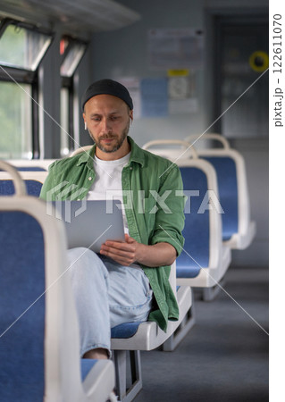 Focused thoughtful man passenger working on laptop while travel by electric train using earphones Focused thoughtful man passenger working on laptop while travel by electric train using earphones 122611070