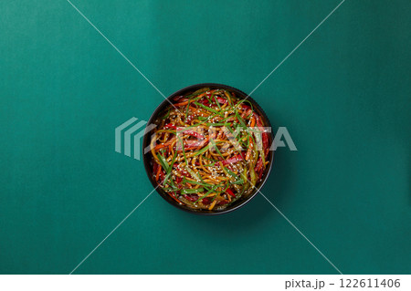 on green background, a black round bowl of rice noodles with striped vegetables sprinkled with sesame seeds, traditional Chinese cuisine on green background, a black round bowl of rice noodles with striped vegetables sprinkled with sesame seeds, traditional Chinese cuisine 122611406