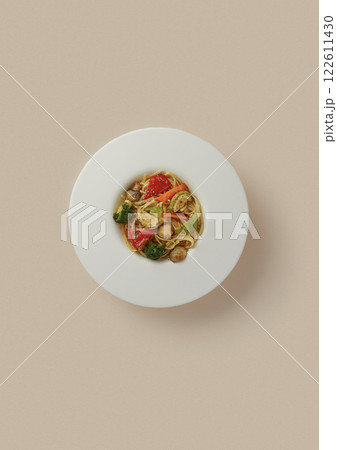on beige background, a round white plate with pasta and grilled vegetables, mushrooms, zucchini, peppers and milk, a lot of carbohydrates and fiber, Italian cuisine 122611430