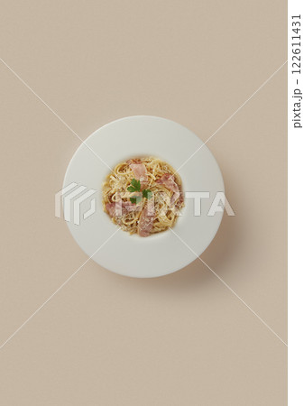 on beige background round white plate with Italian carbonara pasta with cheese and bacon, classic creamy dressing, durum wheat, food rich in carbohydrates and protein 122611431